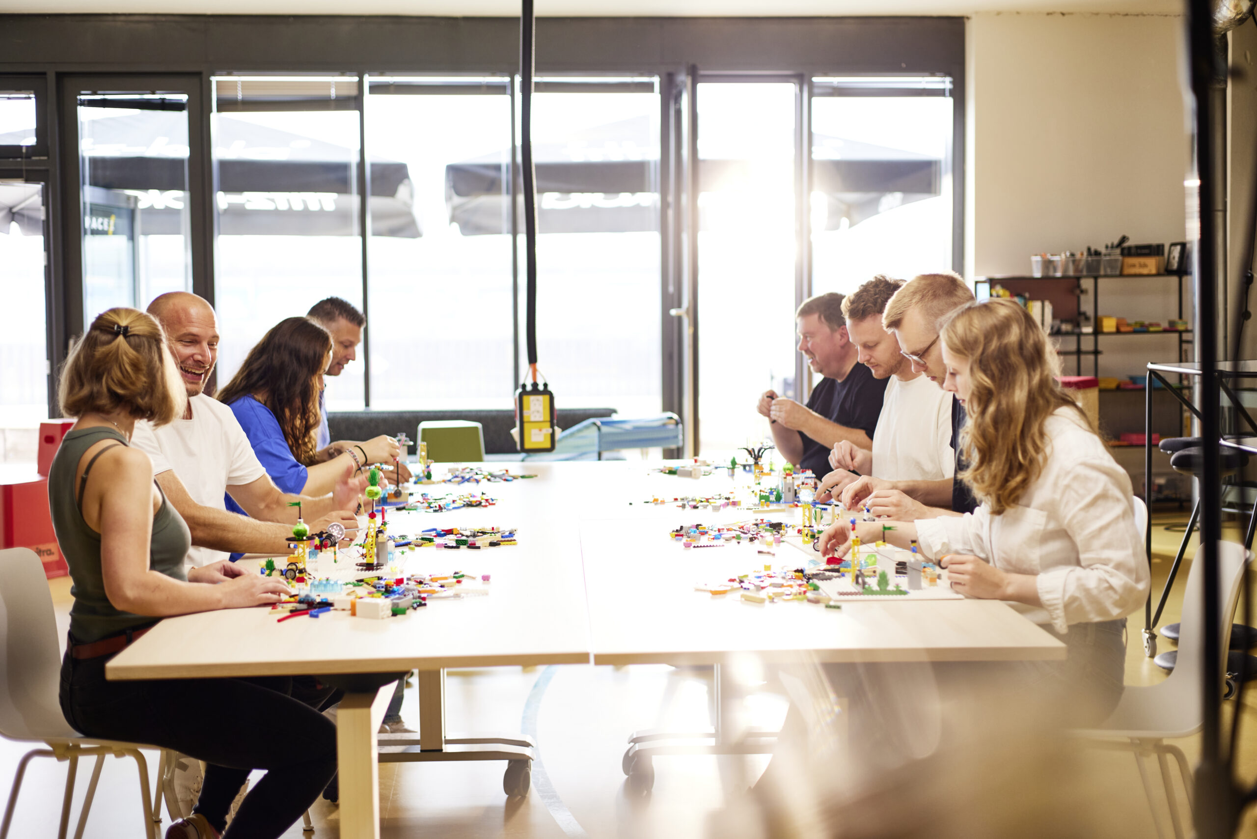 Mehrere Personen arbeiten gemeinsam an einem großen Tisch mit Lego-Steinen.