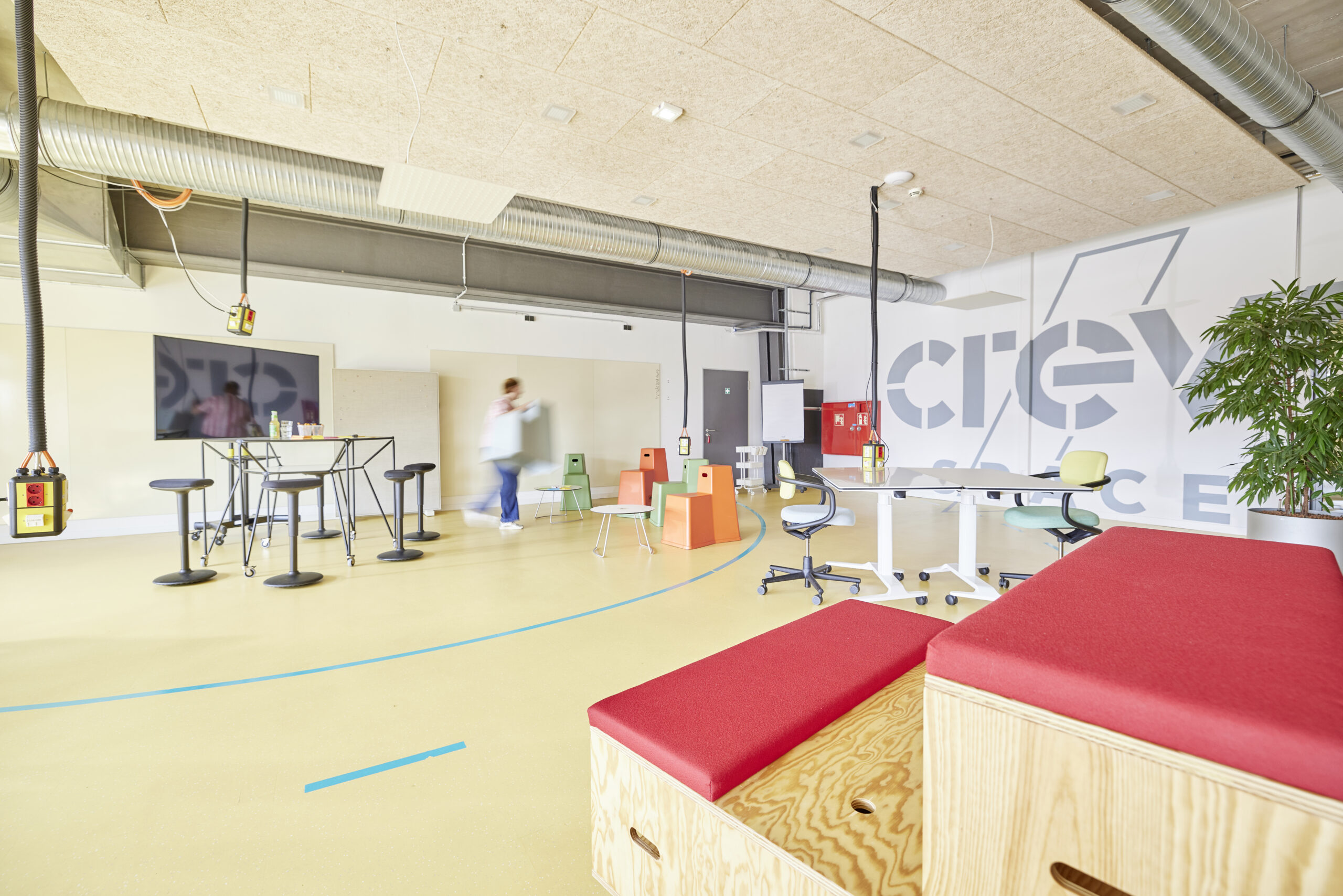 Moderner Workshopraum mit Whiteboards, Sitzgelegenheiten und CREW Space Logo an der Wand; eine Person trägt einen Stuhl.